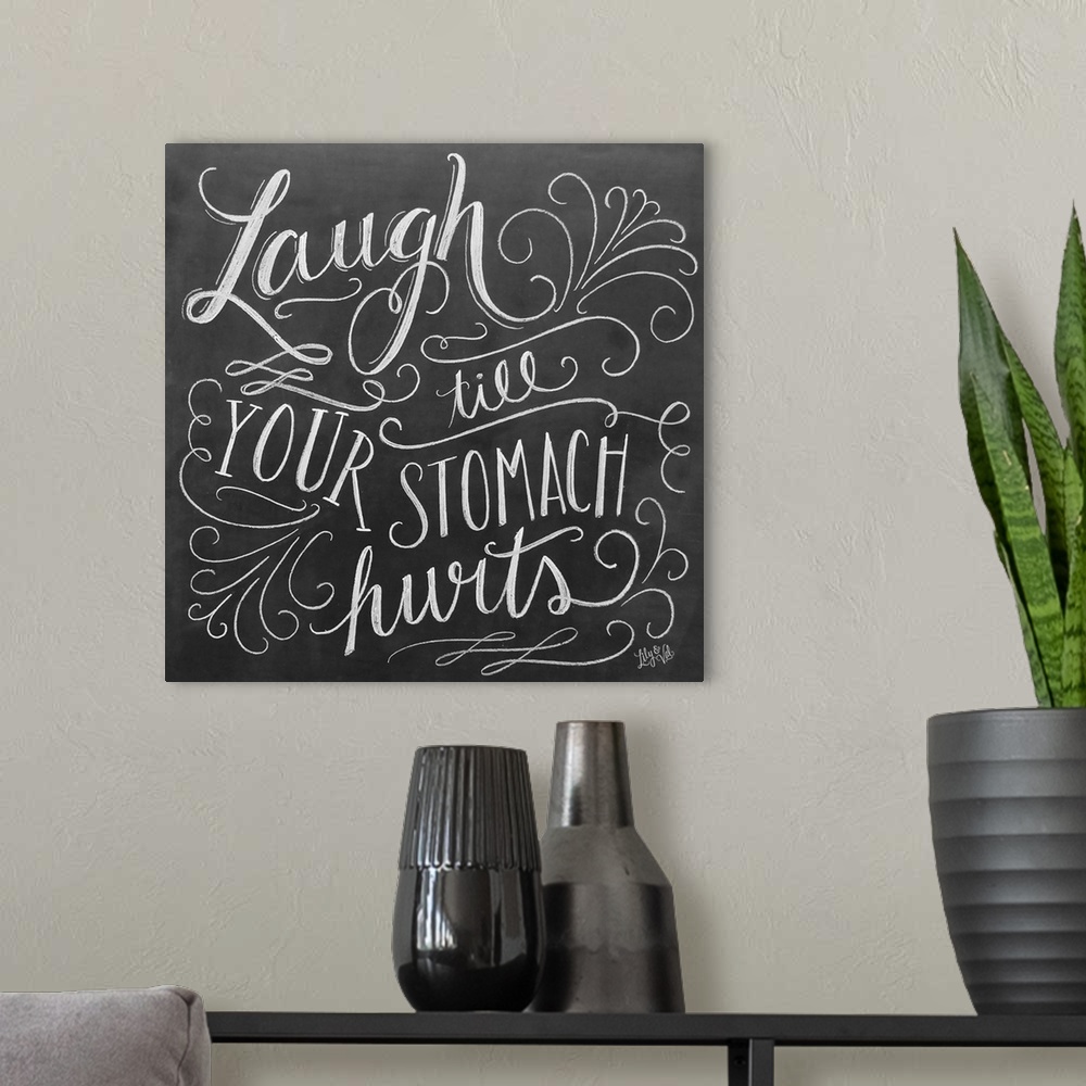 A modern room featuring The phrase "Laugh till your stomach hurts" done in flowing hand-lettering in white chalk on a dar...