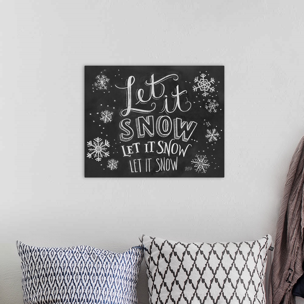 A bohemian room featuring "Let it snow" handwritten with several snowflakes in white chalk on a black background.
