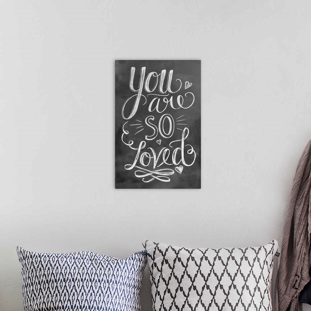 A bohemian room featuring The phrase "You are so loved" done in flowing hand-lettering in white chalk on a dark background.