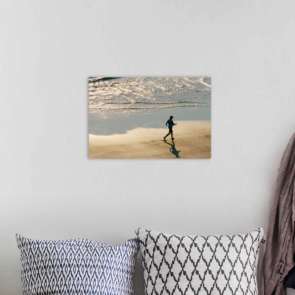 A bohemian room featuring A jogger in silhouette runs on the surf line of the beach as the morning light begins to rise.