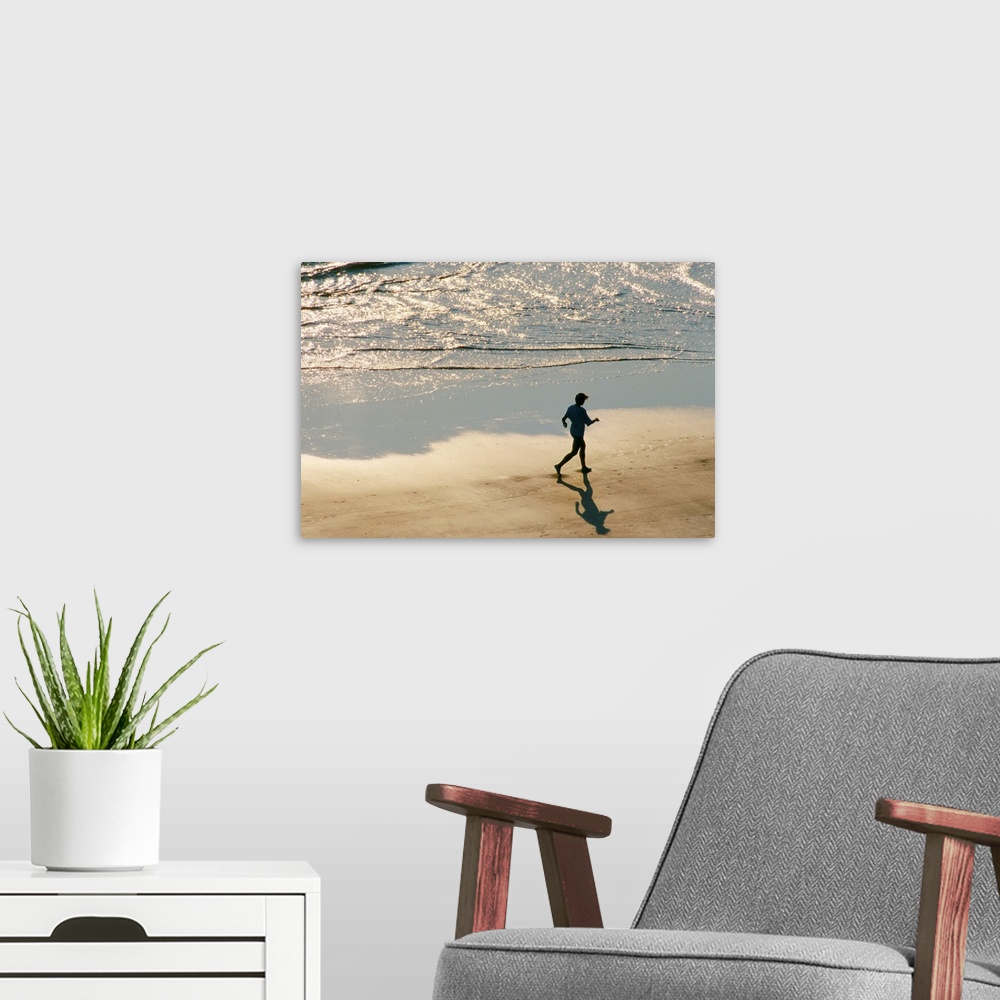 A modern room featuring A jogger in silhouette runs on the surf line of the beach as the morning light begins to rise.