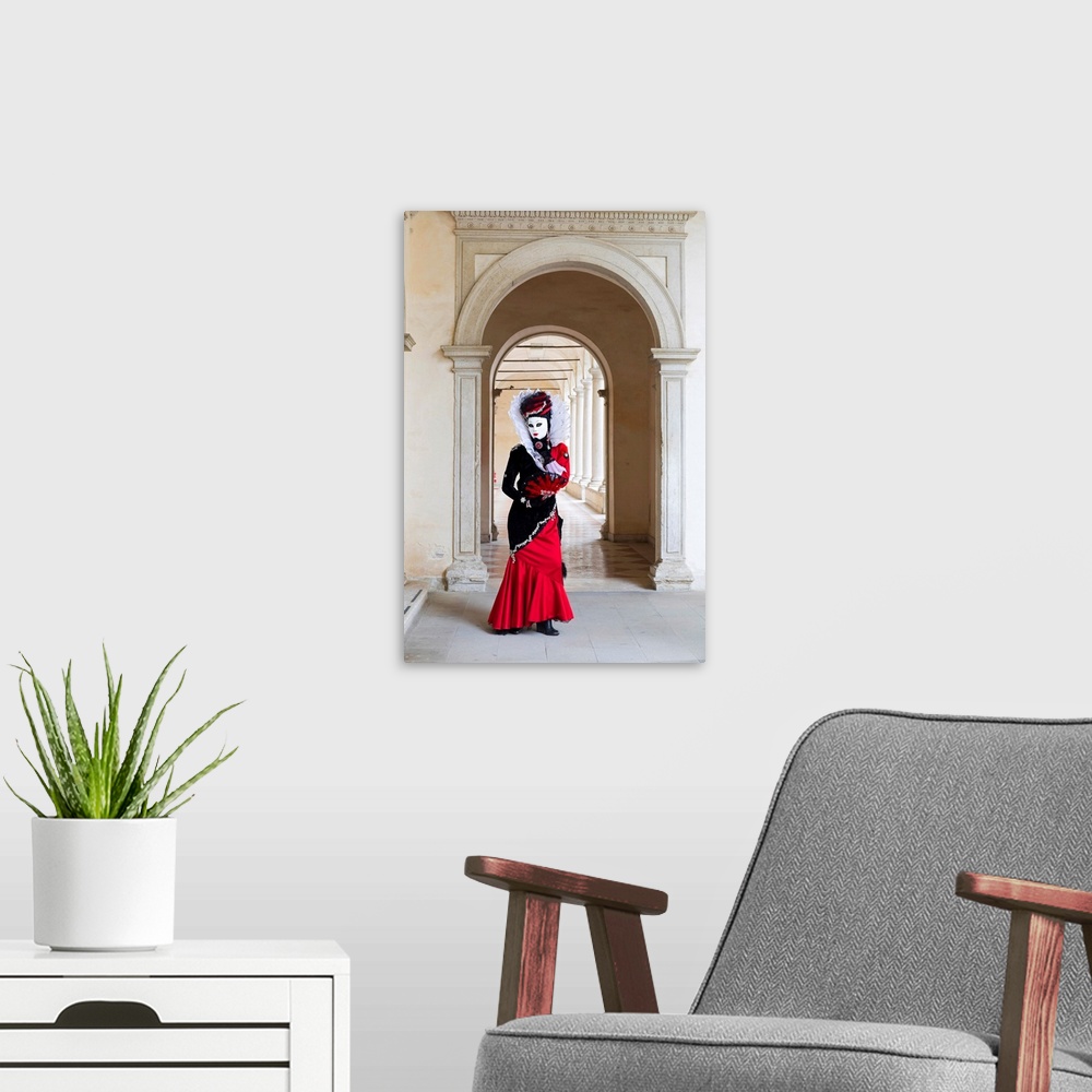 A modern room featuring A Woman In A Red Costume And Mask Poses In An Archway During The Venice Carnival, Venice, Italy