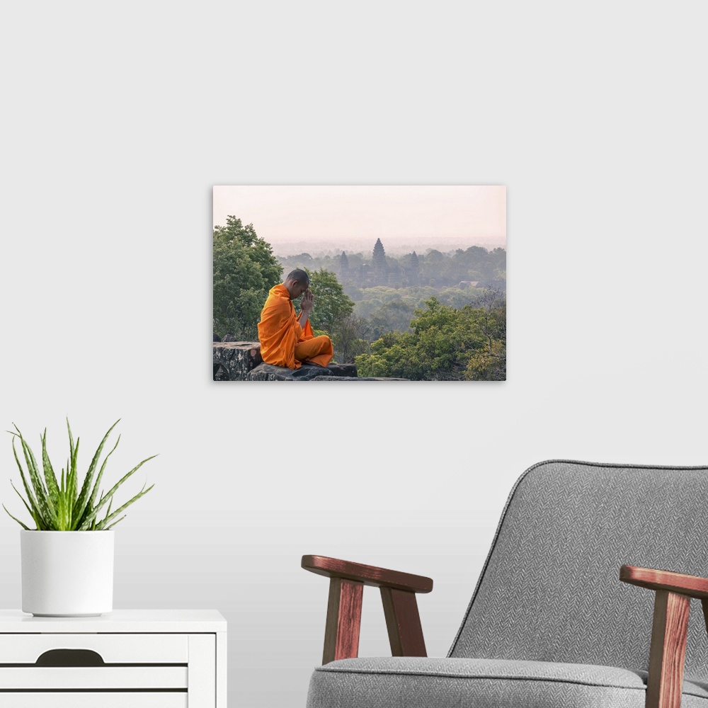 A modern room featuring Cambodia, Siem Reap, Angkor Wat complex. Monk meditating with Angor wat temple in the background ...