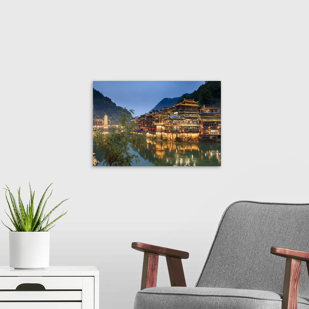 A modern room featuring China, Hunan province, Fenghuang, riverside houses by night reflecting in the river.