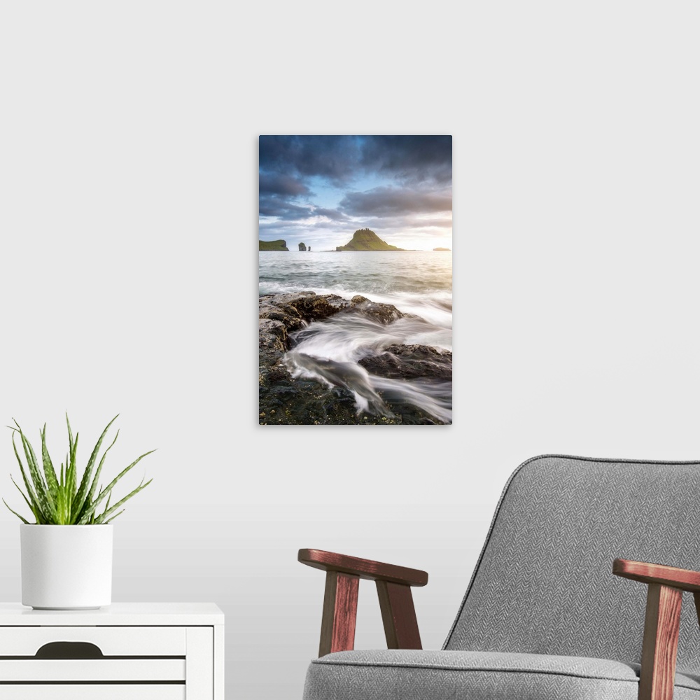 A modern room featuring Vagar island, Faroe Islands, Denmark. Coastal rocks with Tinholmur islet at the background at sun...