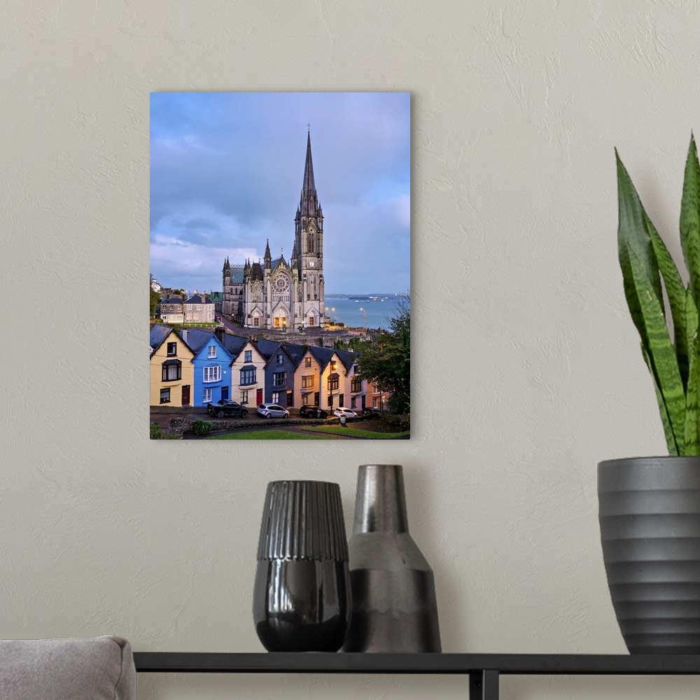 A modern room featuring Deck of Cards colourful houses and St. Colman's Cathedral at dusk, elevated view, Cobh, County Co...