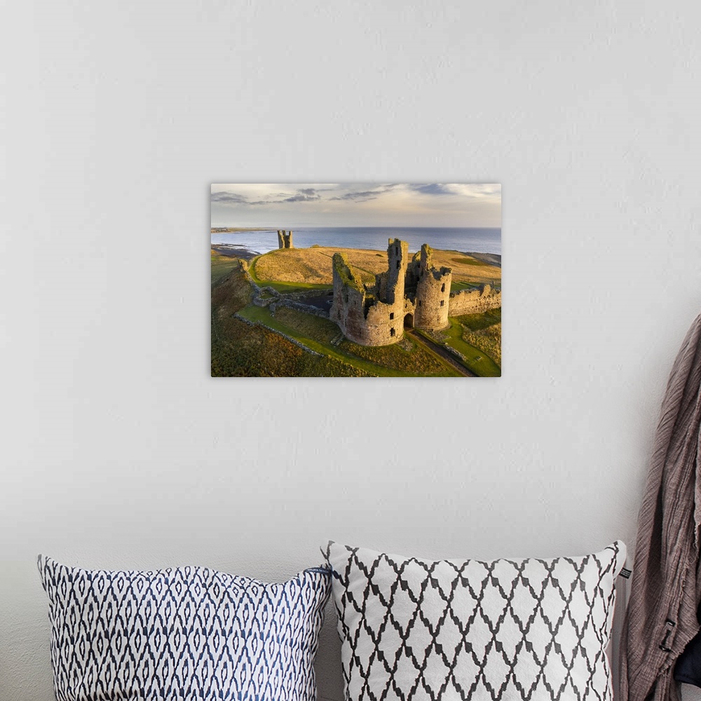 A bohemian room featuring Dunstanburgh Castle's great gatehouse and Lilburn Tower illuminated in early morning sunlight, No...