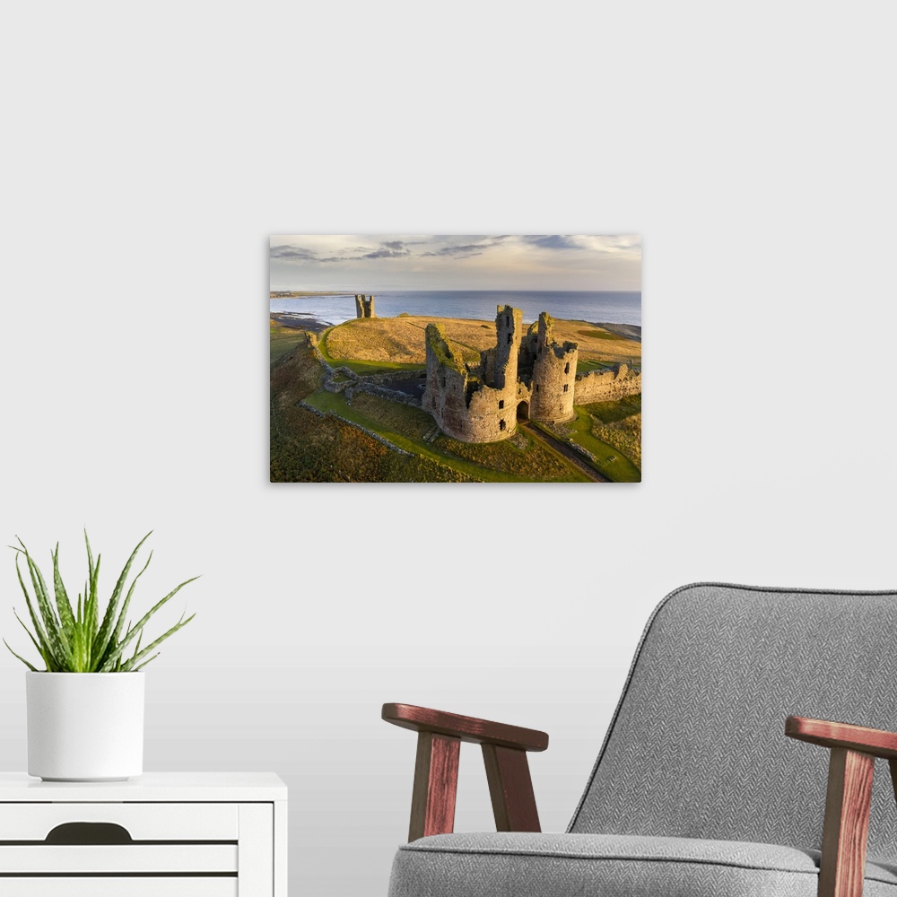 A modern room featuring Dunstanburgh Castle's great gatehouse and Lilburn Tower illuminated in early morning sunlight, No...