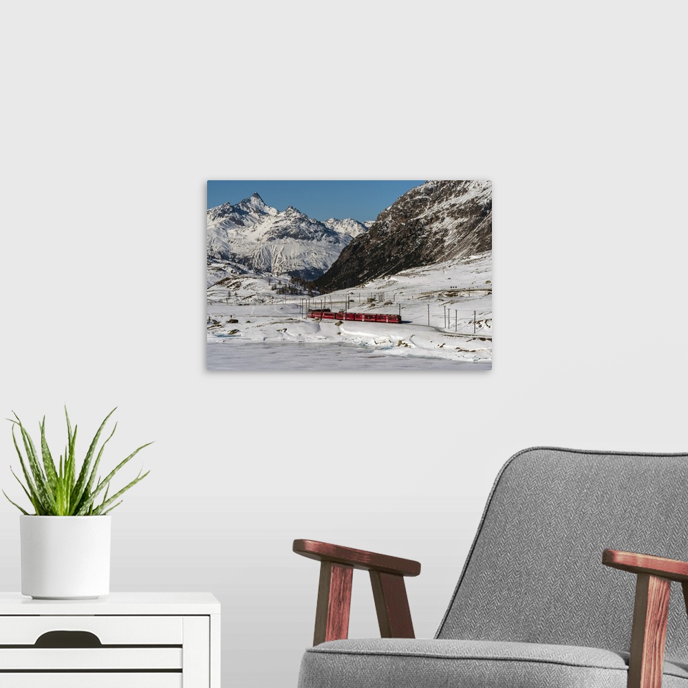 A modern room featuring The famous Bernina Express red train passing Lago Bianco in a scenic winter mountain landscape, G...