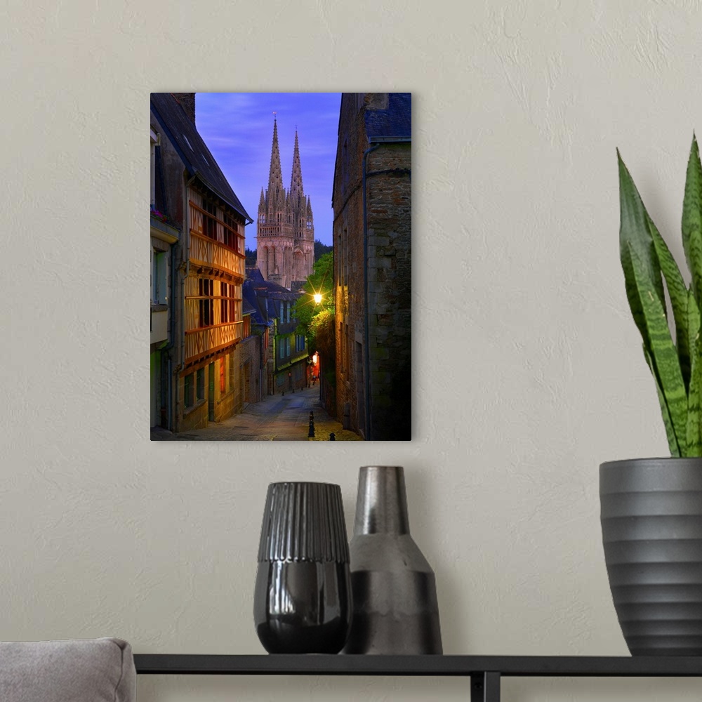 A modern room featuring France, Brittany, Finistere, Quimper, view down cobbled street to Saint Corentin cathedral at dusk.