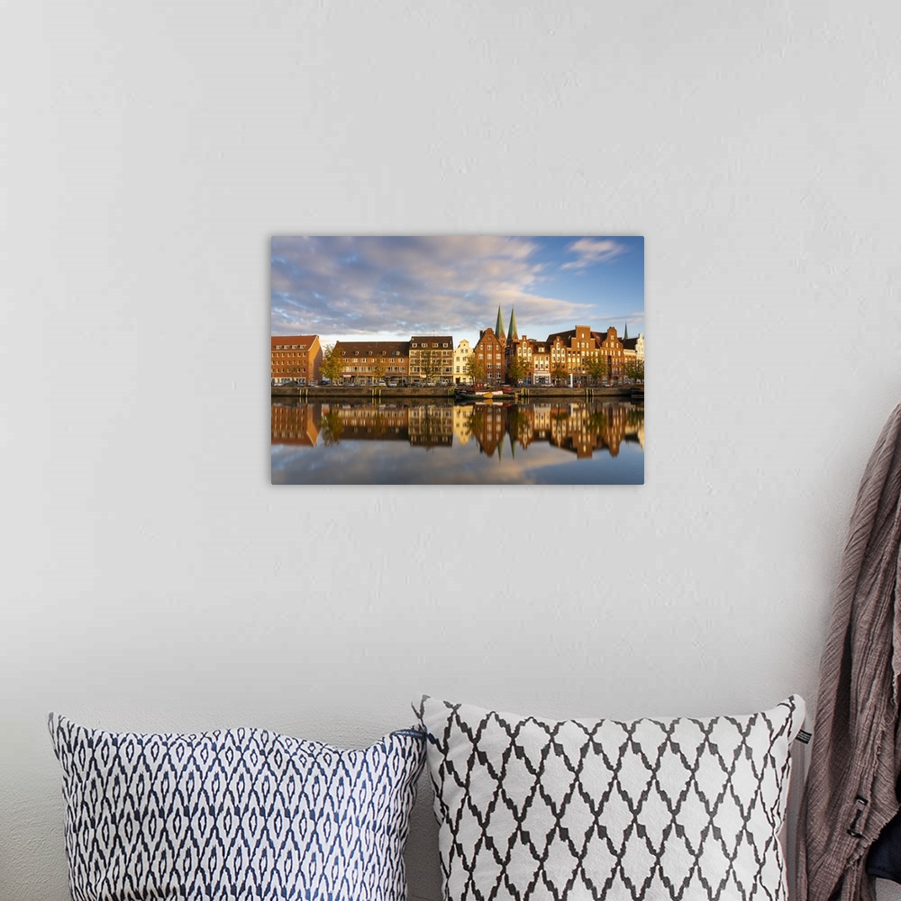 A bohemian room featuring Houses on riverfront of Trave river with towers of St. Marienkirche church in background at sunse...