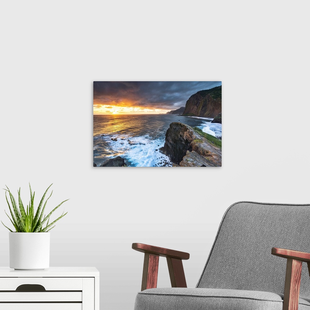 A modern room featuring Man on cliffs looking at waves at dawn, Miradouro Do Guindaste viewpoint, Madeira island, Portugal.