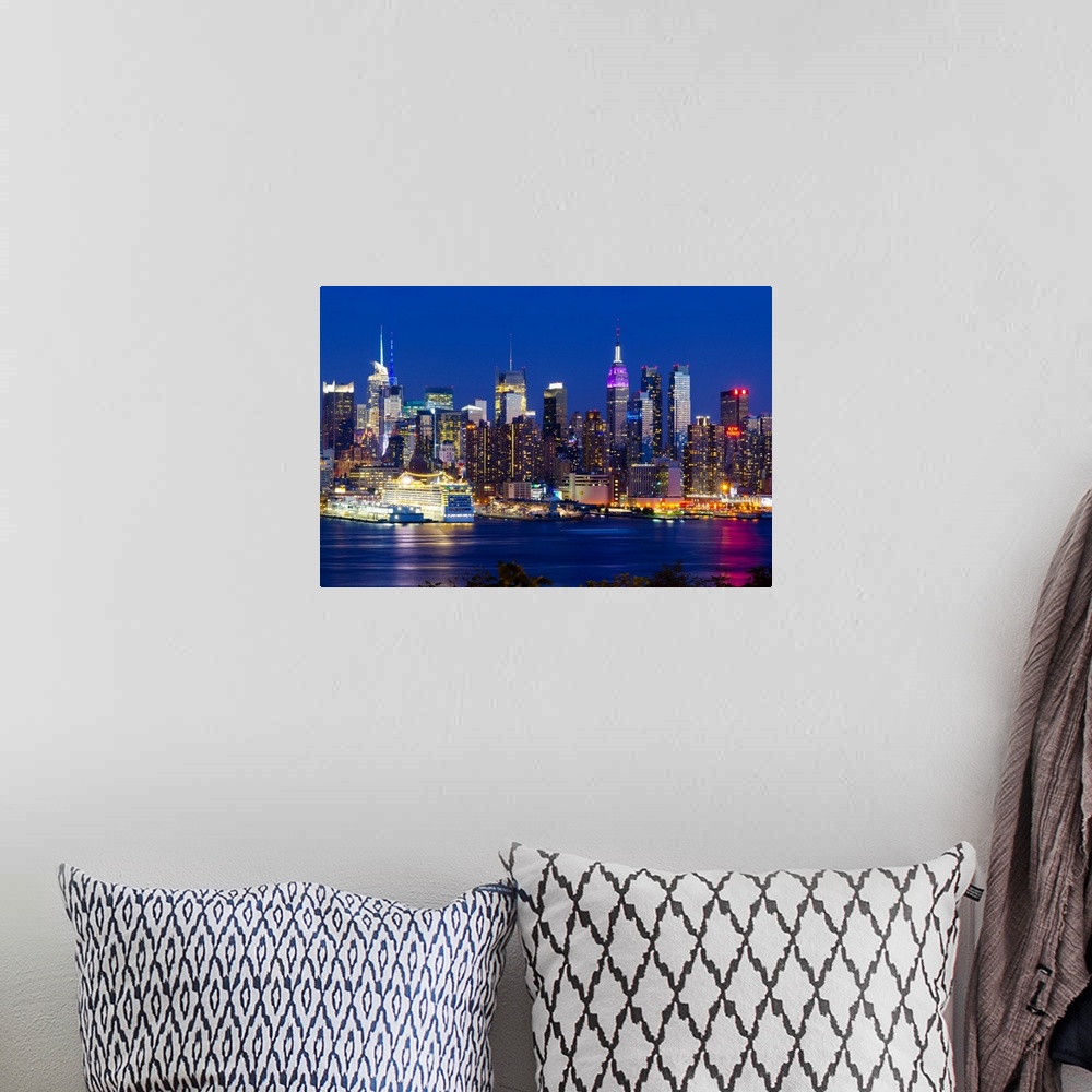 A bohemian room featuring Canvas print of the NYC cityscape lit up in colored lights along a waterfront.