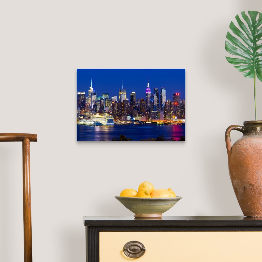 A traditional room featuring Canvas print of the NYC cityscape lit up in colored lights along a waterfront.