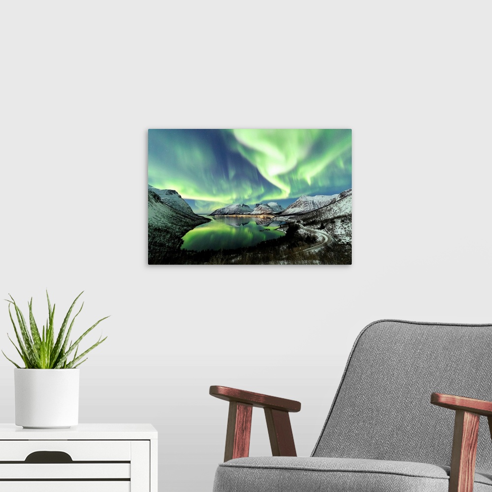 A modern room featuring Northern lights and stars light up the snowy peaks reflected in the cold sea Bergsbotn Senja Trom...