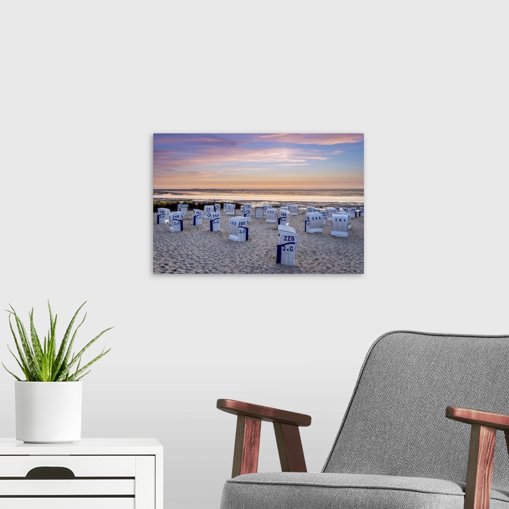 A modern room featuring Duhnen, Cuxhaven, Lower Saxony, Germany. Strandkorb beach chairs and the Wadden Sea at sunset.