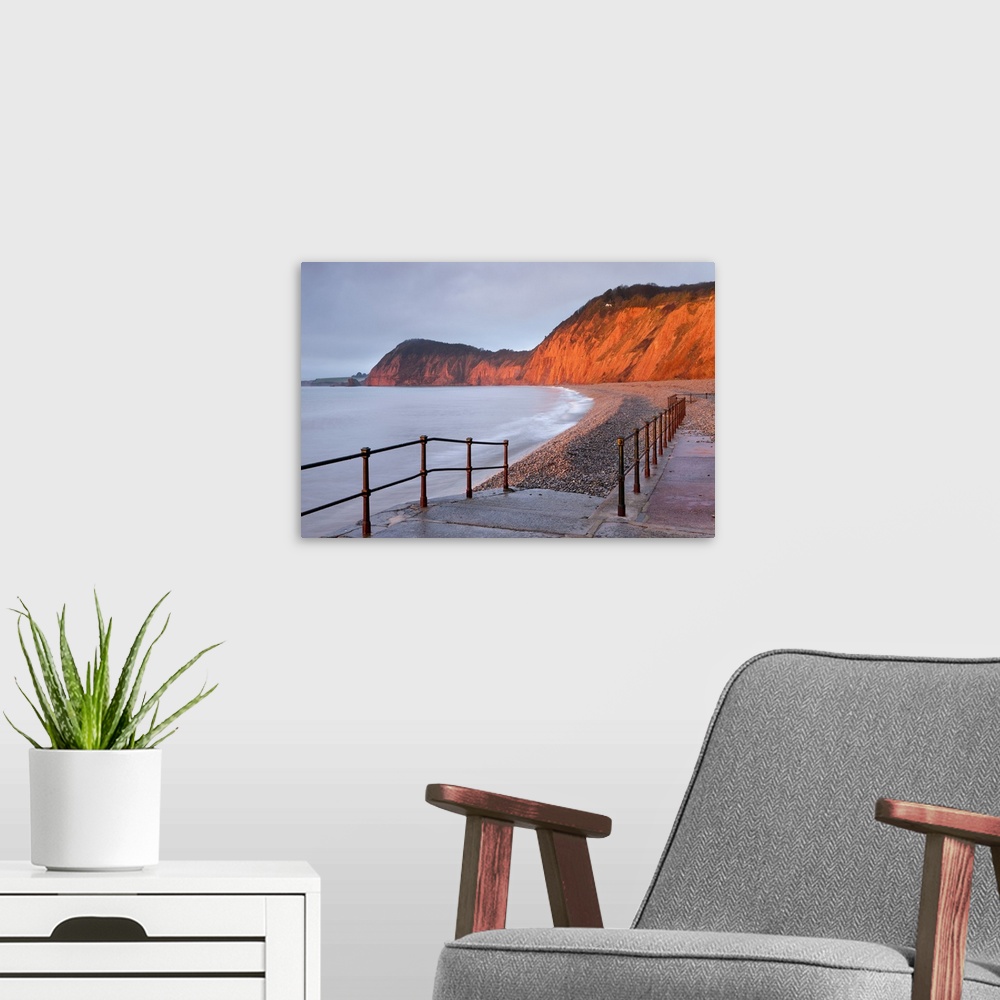 A modern room featuring Early morning sunlight glows against the distinctive red cliffs of High Peak, viewed from the bea...