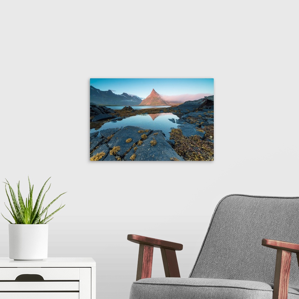 A modern room featuring The rocky peak of Volanstinden lighted up by the midnight sun is reflected in blue sea Fredvang L...