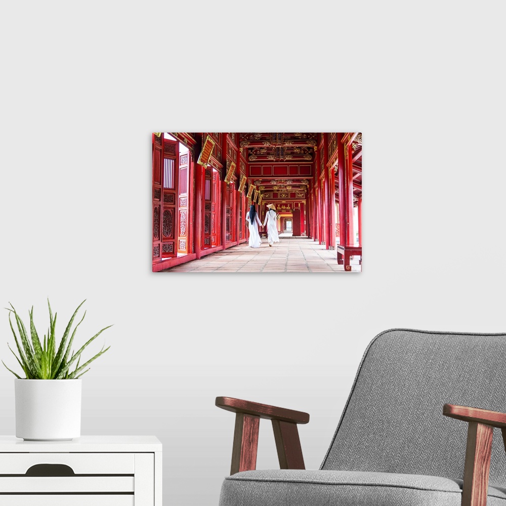 A modern room featuring Two young women wearing traditional national costume, ao dai, in the Imperial City, Hue, Vietnam.