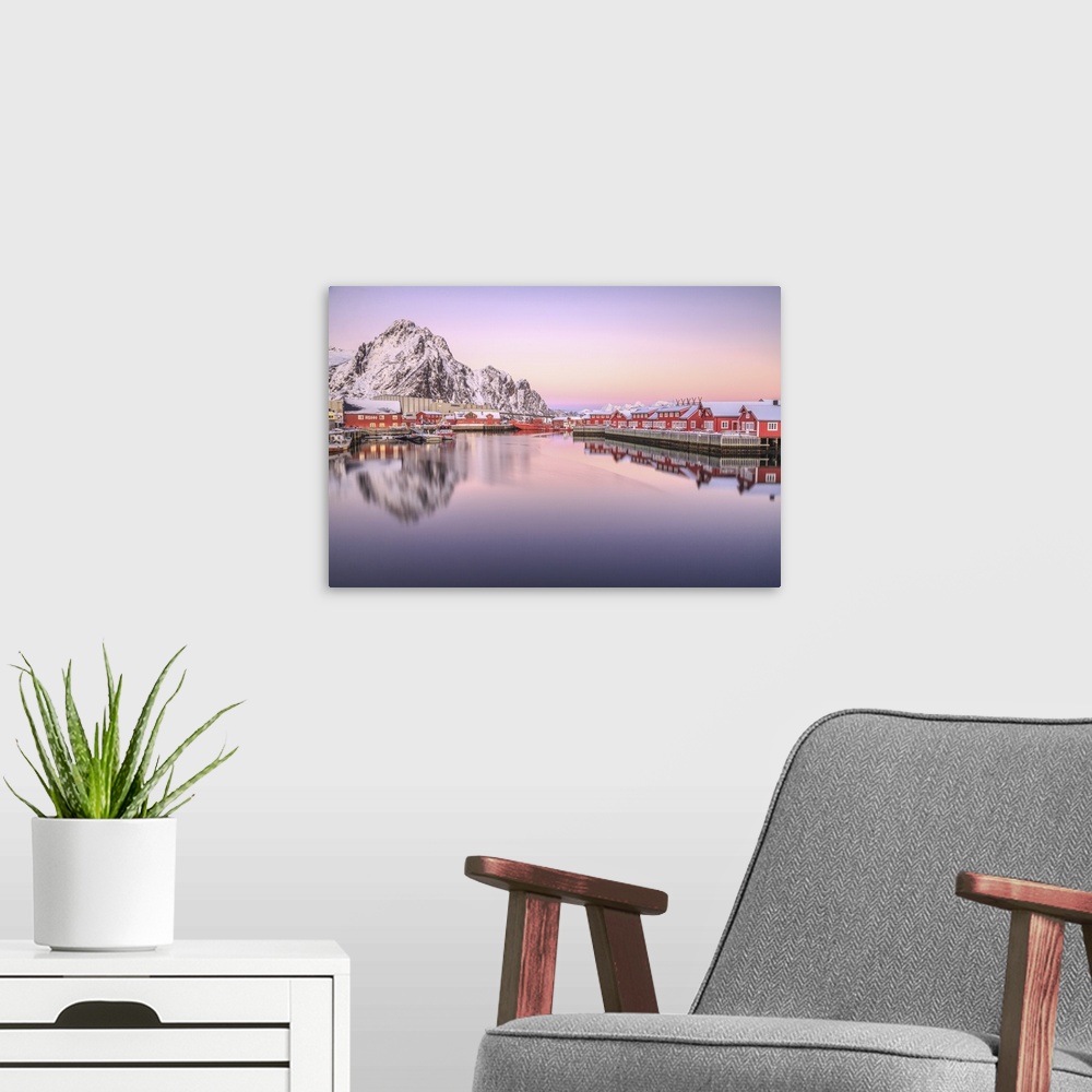 A modern room featuring Pink sunset over the typical red houses reflected in the sea. Svollvaer Lofoten Islands Norway Eu...