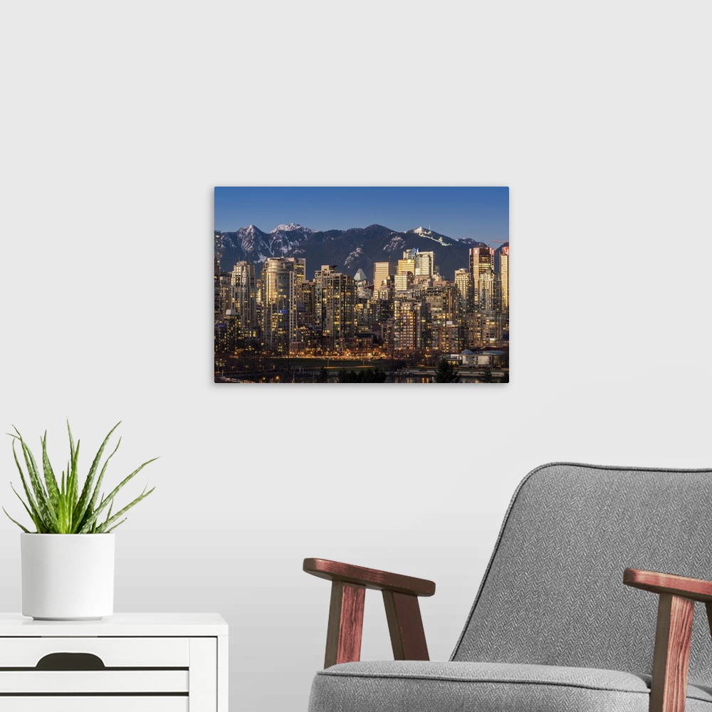 A modern room featuring Downtown skyline with snowy mountains behind at dusk, Vancouver, British Columbia, Canada.