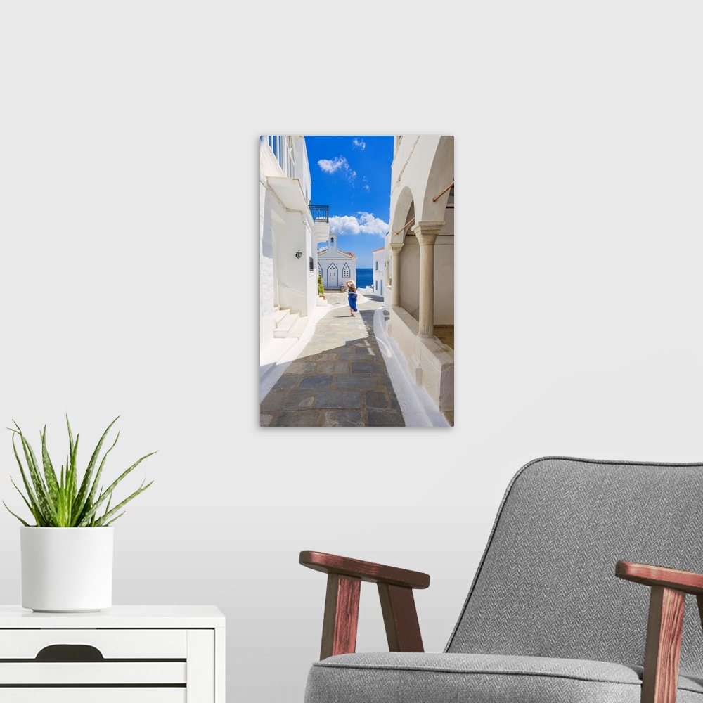 A modern room featuring Young woman walking on the street that leads to the Church of St. Barbara, Andros, Cyclades archi...