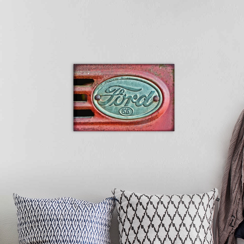 A bohemian room featuring Oversized, horizontal photograph of a Ford emblem attached to an old, rusty 1930's Ford F38.