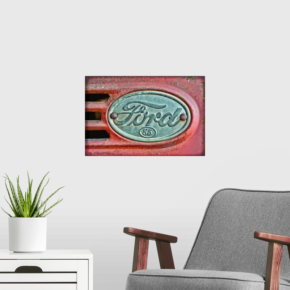 A modern room featuring Oversized, horizontal photograph of a Ford emblem attached to an old, rusty 1930's Ford F38.