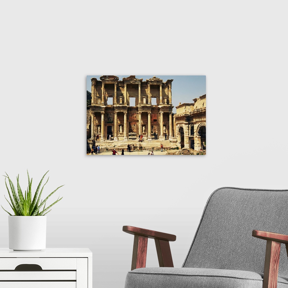 A modern room featuring Tourists gather around the archaeological remains of the Library of Celsus; Ephesus, Turkey. Ephe...