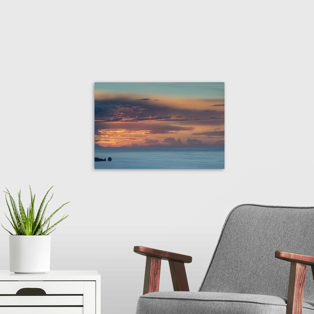 A modern room featuring Photograph of clouds and ocean boulders casting silhouettes from the sun setting in the distance.