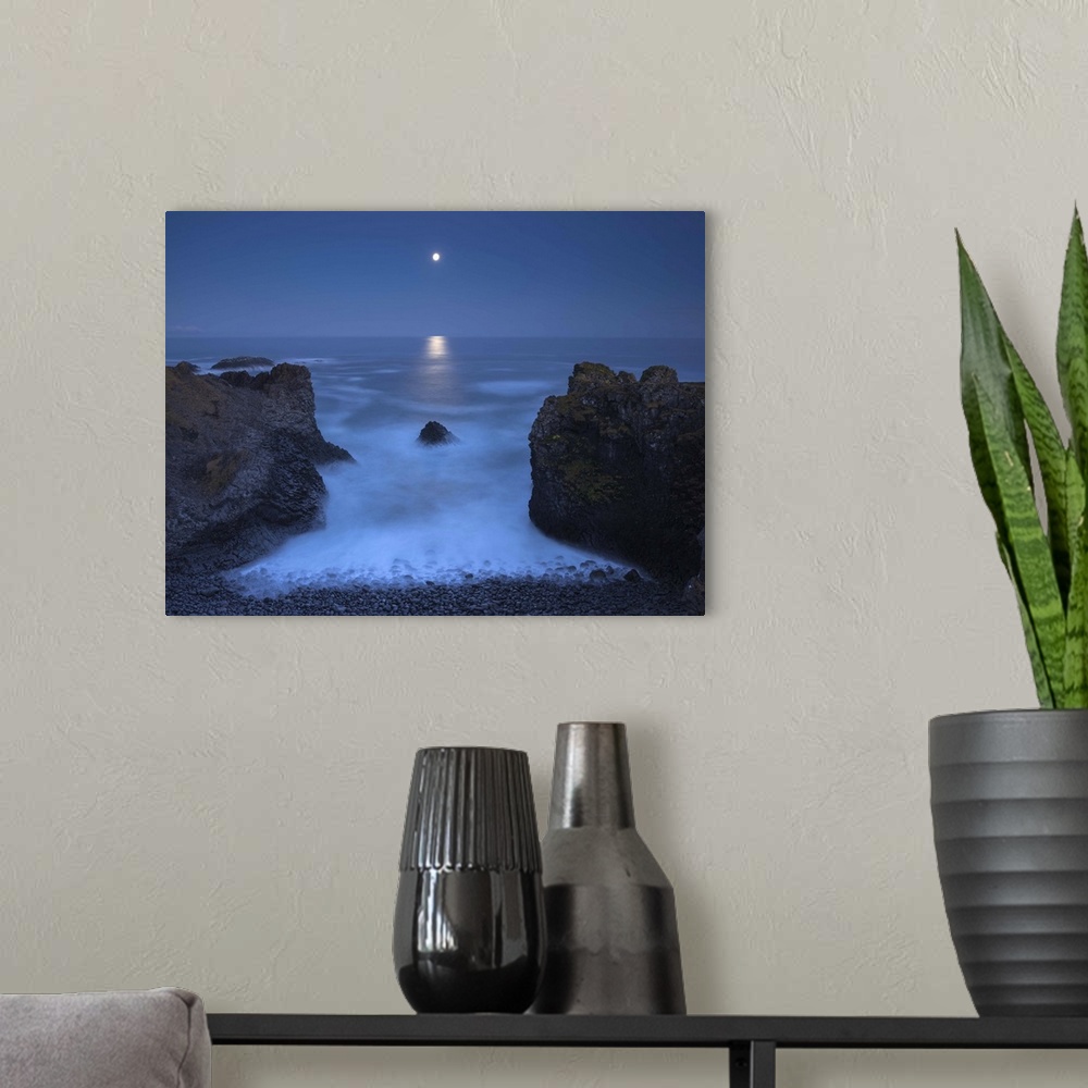 A modern room featuring Illuminated moon in the distance hanging over the ocean in the distance, with two bookend boulder...