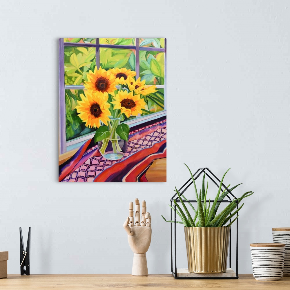 A bohemian room featuring Sunflowers in glass vase on table with plants visible through window.