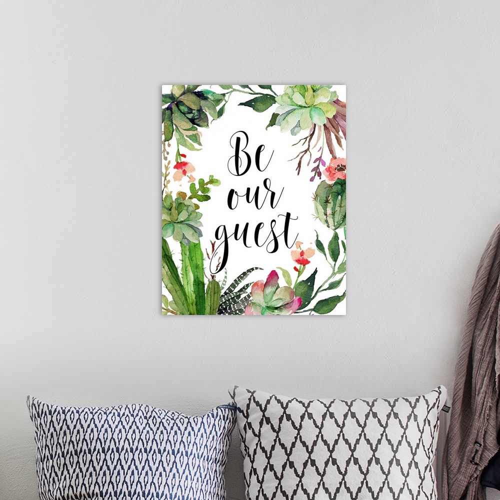 A bohemian room featuring A beautiful watercolor painted wreath with the phrase "Be Our Guest" written in the middle in black.