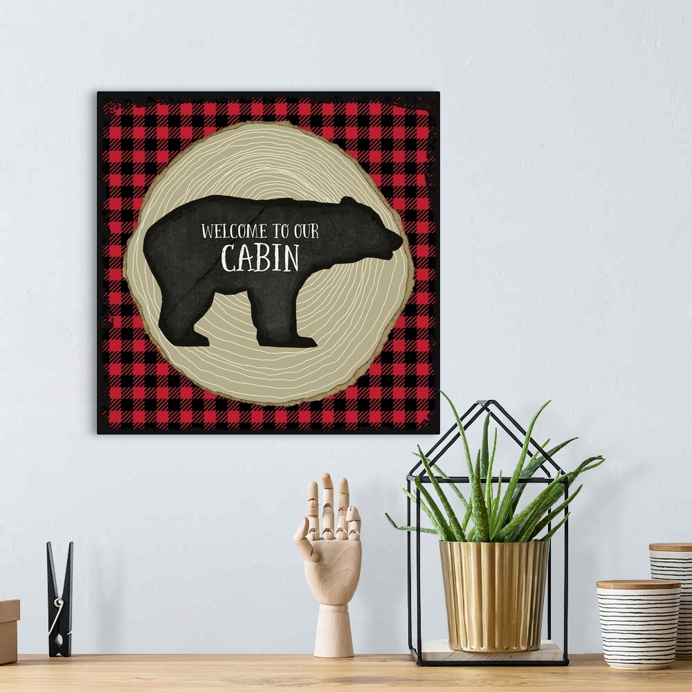A bohemian room featuring "Welcome to Our Cabin" on a bear silhouette over red and black plaid and tree rings.