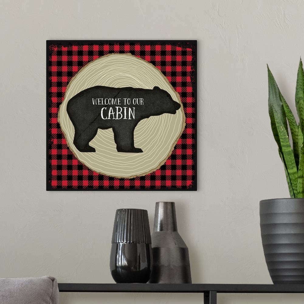 A modern room featuring "Welcome to Our Cabin" on a bear silhouette over red and black plaid and tree rings.