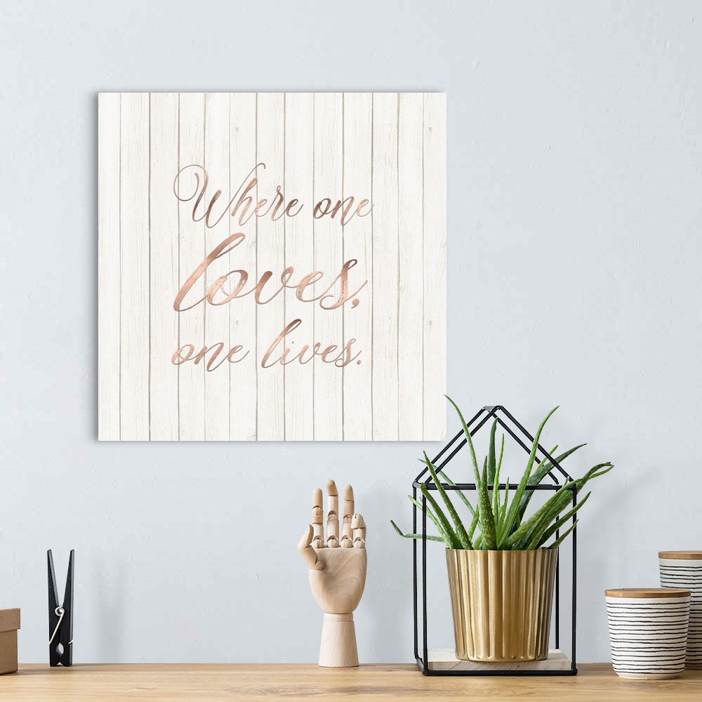 A bohemian room featuring "Where One Loves, One Lives." written in rose gold on a wood paneled background.