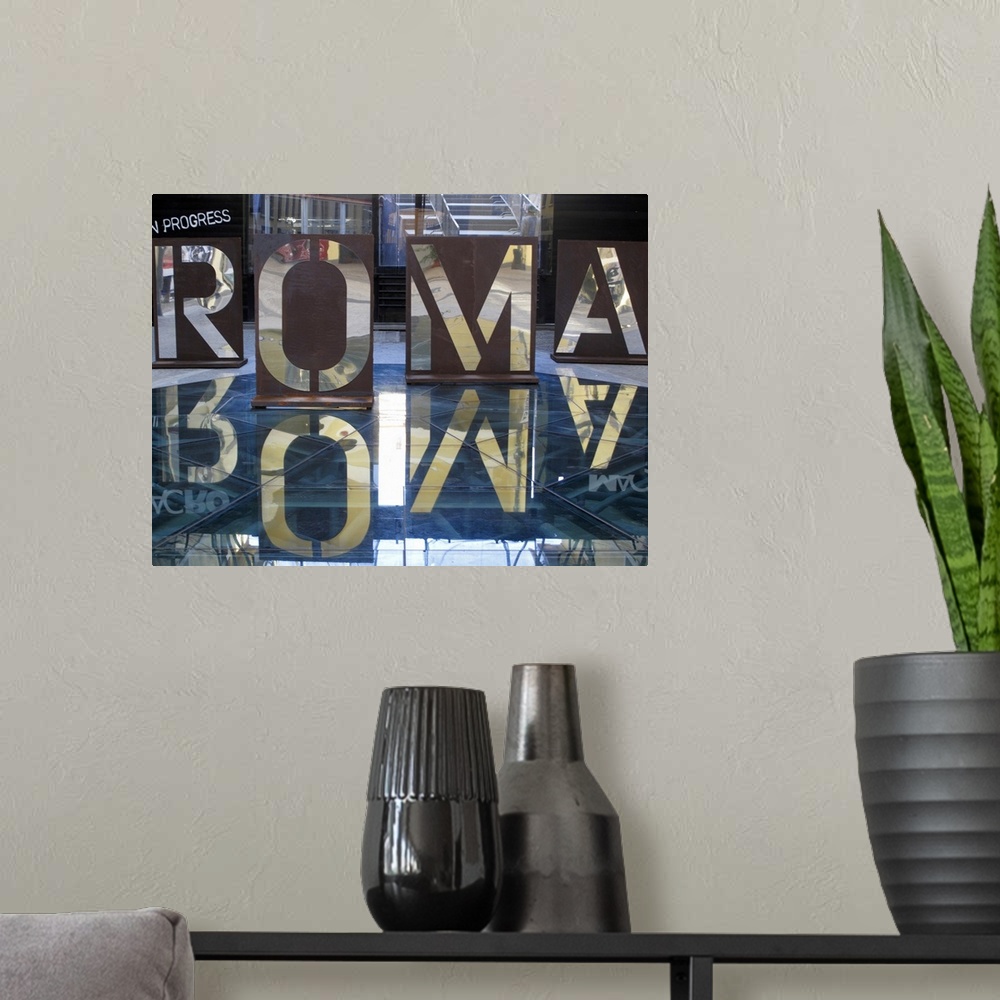 A modern room featuring An interior photograph of letters, that are the Italian spelling of Rome, cut into steel that are...
