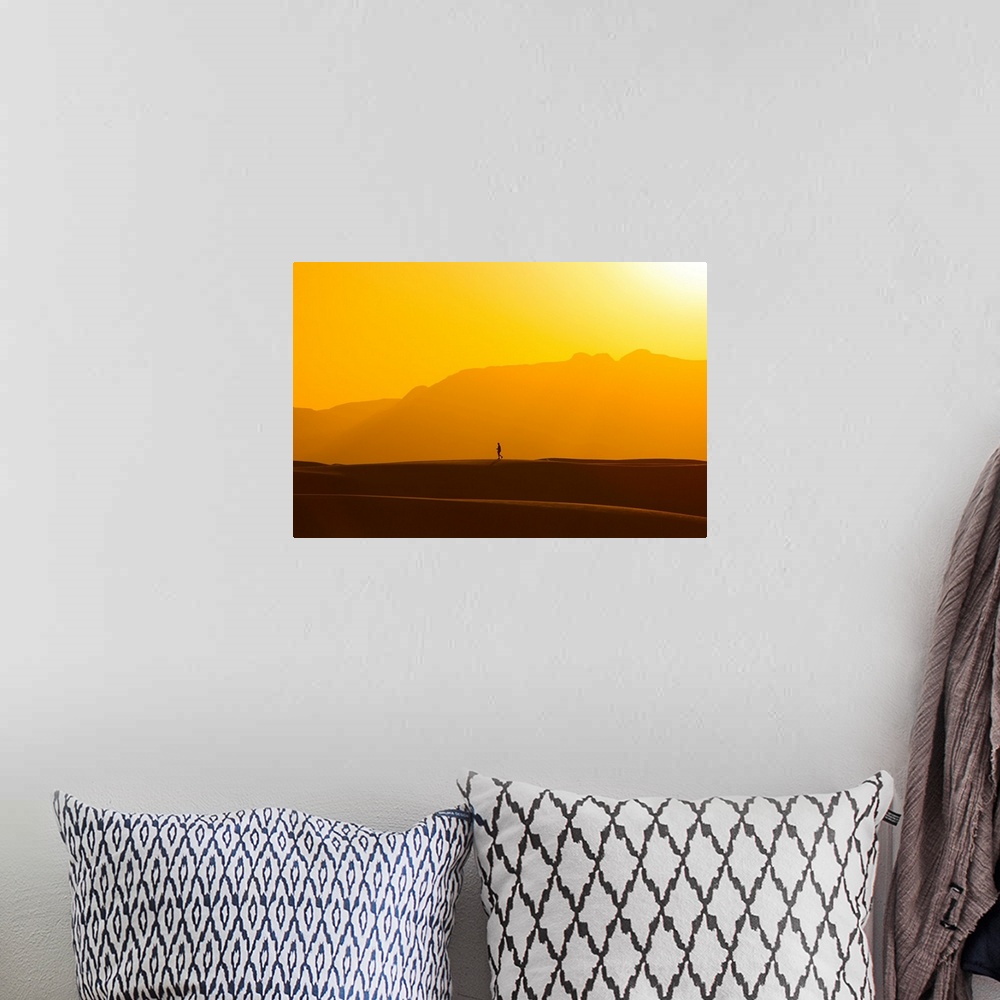 A bohemian room featuring A lone man walks on top of sand dunes during sunset.