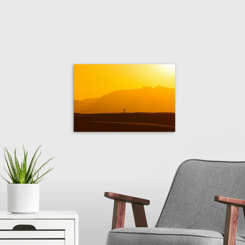 A modern room featuring A lone man walks on top of sand dunes during sunset.