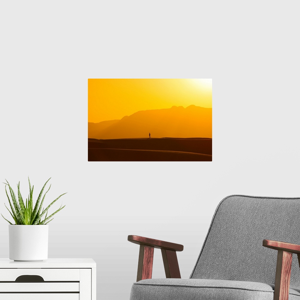 A modern room featuring A lone man walks on top of sand dunes during sunset.