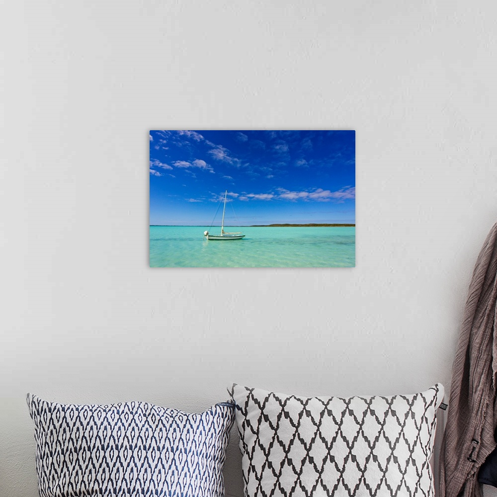 A bohemian room featuring A lone sailboat anchored in turquoise water.