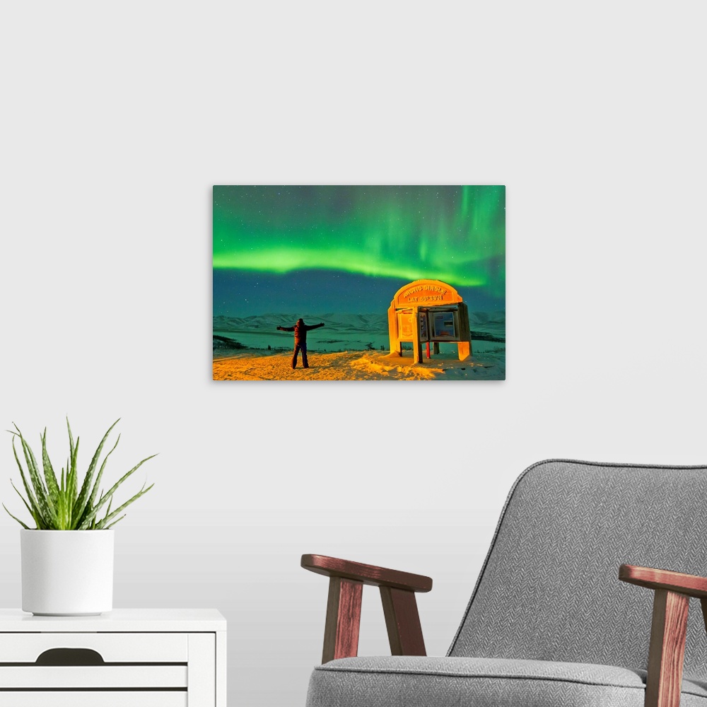 A modern room featuring A man looks in awe at the northern lights near the Arctic Circle sign.