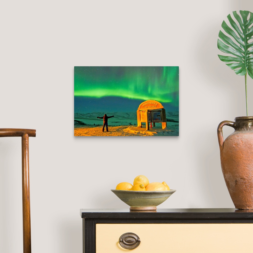 A traditional room featuring A man looks in awe at the northern lights near the Arctic Circle sign.