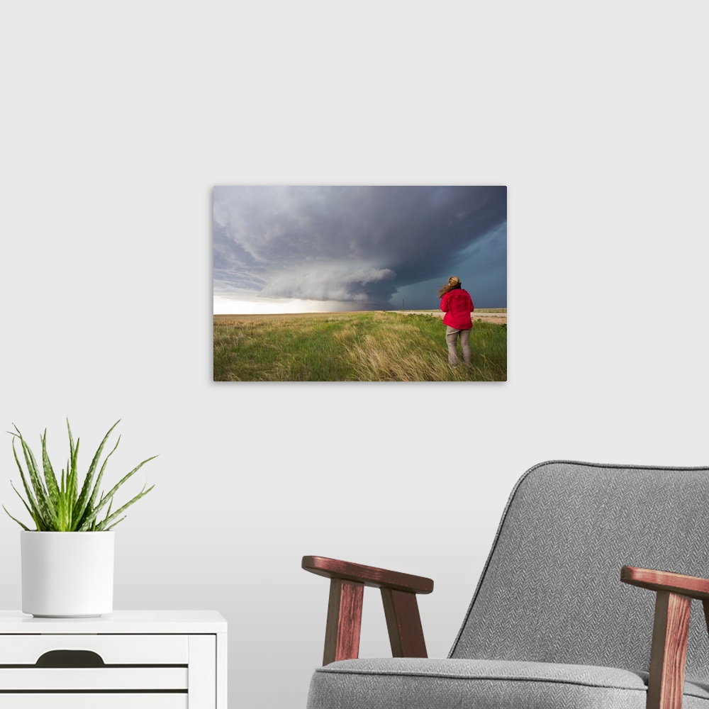 A modern room featuring A woman watches a massive wall cloud from a supercell thunderstorm.