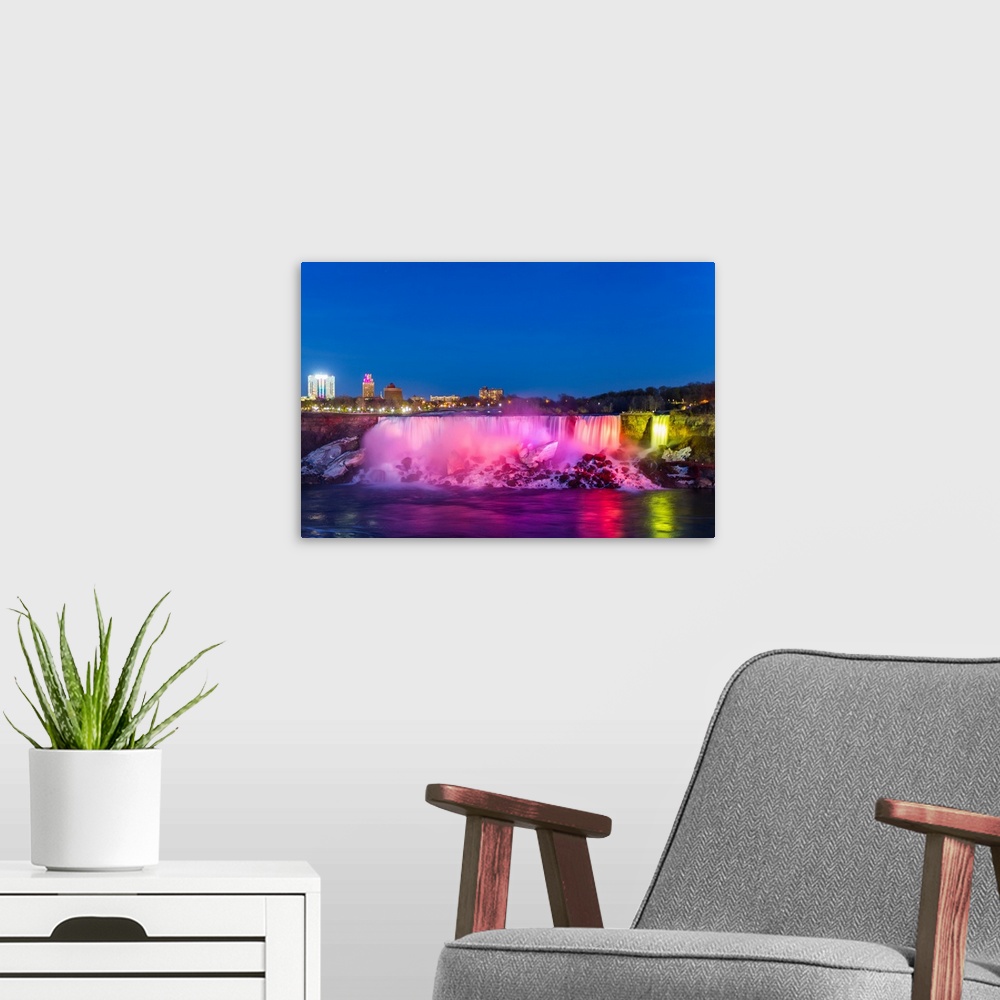 A modern room featuring American Falls illuminated at dusk by colorful lights.