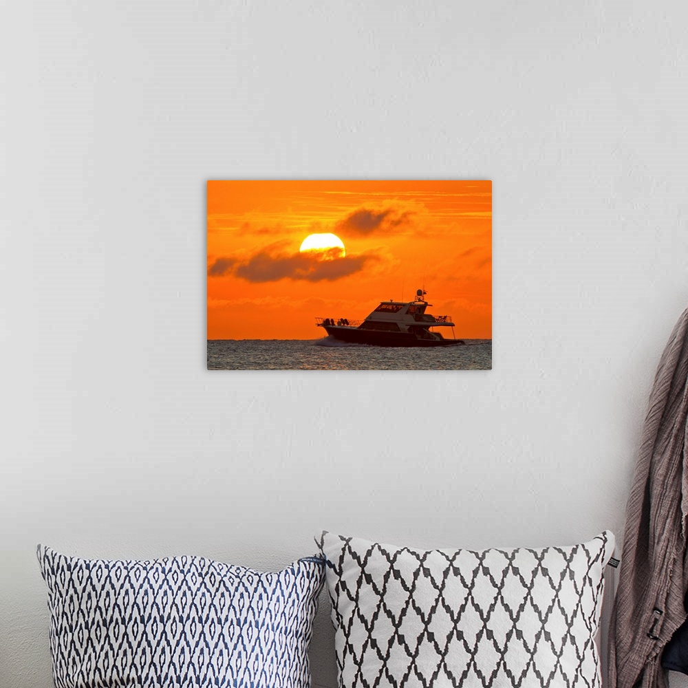 A bohemian room featuring Boat passing in front of a big glowing sun during a spectacular sunset over the Atlantic Ocean.