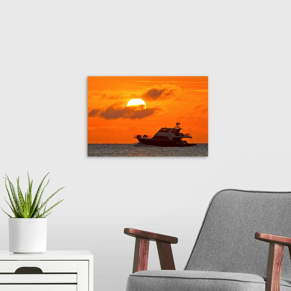 A modern room featuring Boat passing in front of a big glowing sun during a spectacular sunset over the Atlantic Ocean.