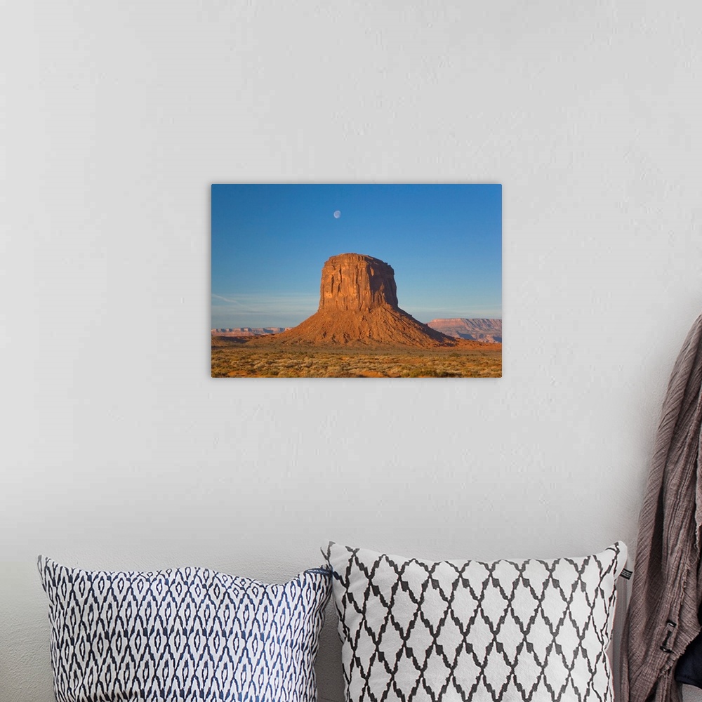 A bohemian room featuring Moon visible over rock formation in Monument Valley in early morning.