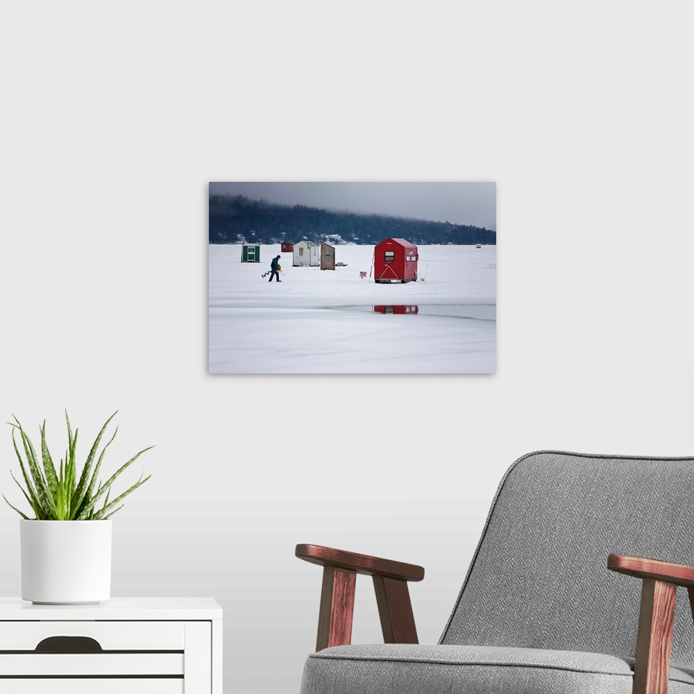 A modern room featuring Ice fisherman with a drill walking among fishing shacks on a frozen lake.