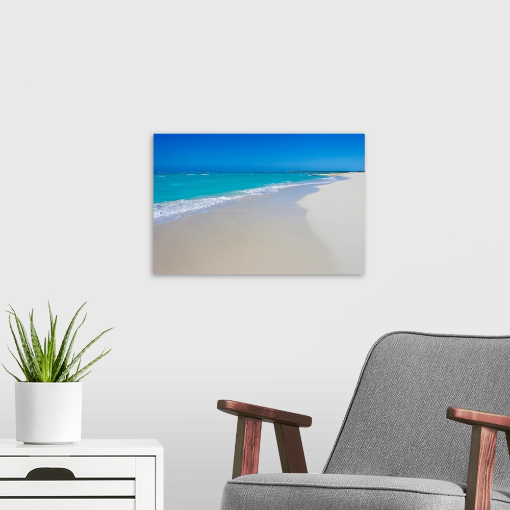 A modern room featuring A beautiful picture of teal colored ocean water coming up onto the white sand beach. A clear blue...